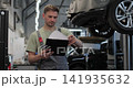 Mechanic man with clipboard walking along workshop. Car service, repair, maintenance and people. 141935632