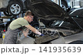 Mechanic talking on a mobile phone with the car owner while repairing a car in a garage. 141935639