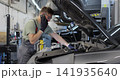 Mechanic talking on a mobile phone with the car owner while repairing a car in a garage. 141935640