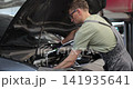Professional mechanic working on a vehicle in a car service. Engine specialist fixing the motor. Repairman is wearing gloves and using a ratchet. 141935641