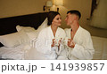 Bride and groom barefoot drinking coffee cups in bed at morning together.  141939857