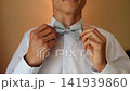 Smiling Caucasian man looking at mirror, fixes bow tie, getting ready for new wedding day 141939860