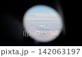 View through an airplane porthole of a cloud layer far below and the horizon line beyond 142063197