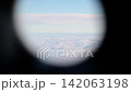 View through an airplane window of a thick layer of white clouds below and blue sky above 142063198