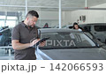 Car salesman filling out paperwork in showroom 142066593
