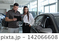 Car salesman consulting female client in dealership showroom 142066608