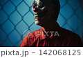 Scary Prisoner With Clown Mask Against Fence Scary Prisoner With Clown Mask Against Fence 142068125