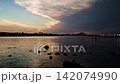 Dramatic time lapse of the 2026 partial solar eclipse totality darkness over Denia coast in Spain. Silhouette of a person standing in the Mediterranean sea watching the sky darken with city lights ref 142074990