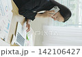 A young Japanese businesswoman talks on her smartphone while working at her desk by a bright window (vertical video). 142106427
