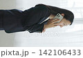 A young Japanese businesswoman smiles and talks on her smartphone by a window (vertical video). 142106433