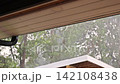 Rain pours down from eaves of building while trees sway in thunder stormy on summer day. 142108438