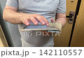 Man in gray shirt holding tablet and tapping screen with fingers near wooden door. Mobile technology, digital device, touchscreen, gadget use. 142110557