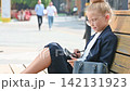 A little girl dressed as a stylish businesswoman sits on a wooden street bench  142131923