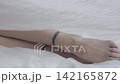 Body beauty and fashion advertisement. Female laying on the bed in the studio. Young woman legs feet close up seminude laying under thin sheet of oilcloth wrap. 142165872