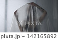 Body beauty and fashion advertisement. Female in underwear sitting on the bed in the studio. Young woman seminude in lingerie sits posing under thin sheet of oilcloth wrap, looks at camera. 142165892