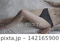 Body beauty and fashion advertisement. Female in underwear laying on the bed in the studio. Young woman seminude in lingerie laying posing under thin sheet of oilcloth wrap, looking at camera. 142165900