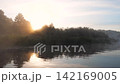 Beautiful early morning sunrise over calm river with gentle mist rising from water and lush green banks. Creating a peaceful and serene natural landscape with perfect reflections 142169005