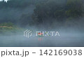 Two people in green kayak are sailing along calm river on foggy morning surrounded by dense forest. Couple in orange life jackets are rafting on a river covered in mysterious fog. Rafting on the river 142169038