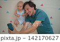 Happy father showing baby on phone beside soft mat. 142170627