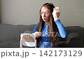 lifestyle video of a young woman wearing glasses, with long dark blonde wet hair, sitting at a table and brushing her damp hair while looking into a mirror. Natural self-care routine and personal groo 142173129