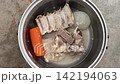 Metal pot with boiled pork bones, carrot and onion in water on concrete floor. Homemade broth, soup cooking, bone meal, pet food preparation. 142194063