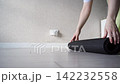 Static Shot Of Person Unrolling Yoga Mat And Standing Barefoot On Mat In Bright Home Exercise Room 142232558