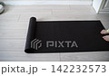 Static Shot Of Person Unrolling Yoga Mat And Stepping Onto It In Bright Home Interior With Light 142232573