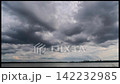 Aerial zoom out cloudscape cloudy sky timelapse over the water of Lake as a storm blows through at dusk just before the sun sets creating orange colored clouds on a blue sky. 142232985