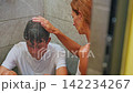 A teenage boy sits in the shower alone water is pouring on him. His mother strokes his head trying to help and calm him down. The kid is feeling upset, emotional, and mentally struggling 142234267