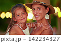 A portrait of a mother in a hat holding her little daughter in her arms. A joyful moment at sunset on the ocean shore 142234327