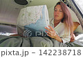 Woman resting on a bed inside a van while studying a map 142238718