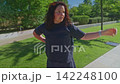 A contemplative moment captured in a serene park, featuring a woman reflecting while checking her watch under the sunlit greenery, signaling thoughts of time and direction. 142248100