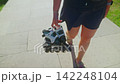 A Person Walking with Rollerblades: Enjoying a Sunny Day Outdoors While Carrying Inline Skates in a Leisurely Stroll by a Paved Pathway 142248104