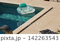 Inflatable pool floats in private villa pool during the summer. Sunlight reflects off surface of the water. Light plays on blue tiled bottom underwater. Gentle breeze. Pula, Croatia - August 15, 2026 142263543