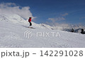 Skier in red jacket skiing down snowy mountain slope in beautiful winter setting, with clear blue skies and majestic alpine peaks creating an exhilarating backdrop. Winter sport. Following to skier 142291028