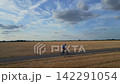 Cyclist Riding Mountain Bike on Asphalt Country Road Through Harvested Field Under Blue Sky 142291054