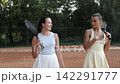 Two young female tennis players standing near the net on an outdoor clay court and having an animated conversation. 142291777