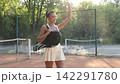 Smiling young woman waving on outdoor clay tennis court 142291780