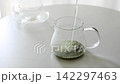 緑茶の茶葉が入った透明なガラス急須にお湯を注ぐ様子・お茶を淹れる 142297463