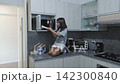 Young girl kneeling on kitchen counter to use the microwave oven 142300840