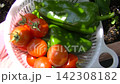 Harvested cherry tomatoes and bell peppers; summer vegetables in a white colander. 142308182
