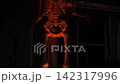 Large skeleton decoration glows orange against a dark suburban house. Bones, ribs, and skull are highlighted with dramatic light for a spooky Halloween scene. 142317996