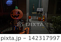 Front porch of a suburban house decorated for Halloween at night with pumpkins, jack-o-lanterns, and orange rope lights. An inflatable pumpkin skeleton stands by a candy table with a sign for trick-or 142317997