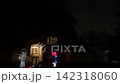 Suburban house at night with a tall inflatable skeleton and a glowing demon pumpkin figure in the yard. Porch lights, windows, and lawn decorations create a spooky neighborhood scene. 142318060