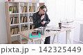 Corporate routine. Office makeup. Female manager talking on smartphone applying face powder at desk with laptop for business paperwork indoor. 142325449