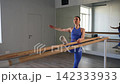 Determined fit female exercising standing split at gymnastic barre in fitness studio, strengthening and flexing back, abdominal and inner and outer thigh during training. 142333933