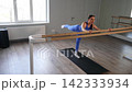 Active flexible sporty female exercising on barre, practicing push-ups paired with straight back leg lift exercise, strengthening upper body, core, glutes, and hamstrings while improving flexibility 142333934