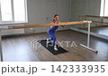 Active flexible elegant fit female exercising on barre, practicing lunge paired with straight back leg lift exercise, stretching hip flexors and strengthening glutes, hamstring and lower back muscles 142333935