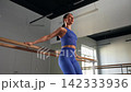 Motivated active sporty woman doing pulse squats at barre in health club, strengthening legs, glutes, and core muscles and improving lower body endurance during indoor workout. 142333936