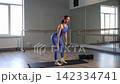 Determined fit sporty pretty woman practicing resistance band deadlift exercise, flexing lower and upper body muscles, strengthening glutes, hamstrings and back during cross training in fitness studio 142334741
